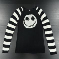 a black and white sweater with a jack skellingy face on the front is laying on a wooden surface