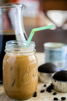 a glass jar with a green straw next to some cupcakes on a table