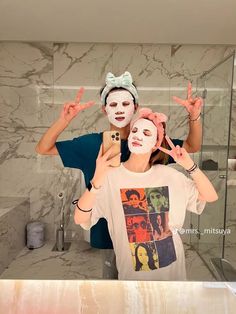 a man and woman are in the bathroom with their faces painted like they are holding up peace signs