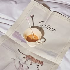 an open magazine with a cup of coffee and spoons on it, sitting on a bed