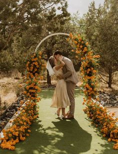 a bride and groom kissing under an orange flower arch