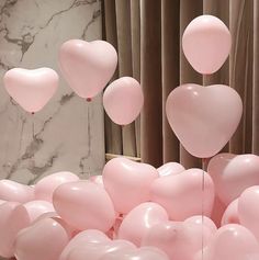 pink balloons are floating in the air near a marble wall and window with drapes