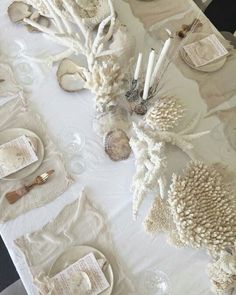 the table is set with white dishes and seashells