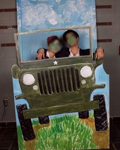 two people in an army jeep painted on the side of a cardboard wall with grass and blue sky behind them