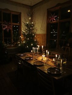 a dining room table set with candles and plates on it in front of a christmas tree