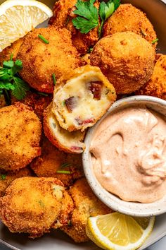 fried food with dipping sauce in a bowl next to lemon wedges and garnish