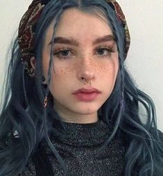 a woman with blue hair and piercings wearing a black top is looking at the camera