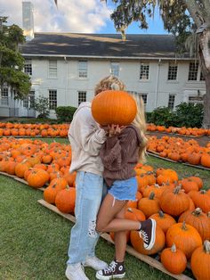 two people standing next to each other with pumpkins in front of them on the grass