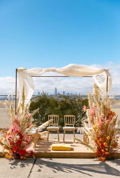 an outdoor ceremony setup with chairs and flowers on the ground in front of a cityscape