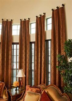 a living room filled with lots of furniture next to tall windows covered in brown curtains