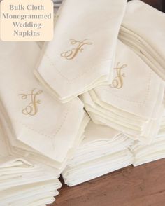 a stack of folded white napkins with monogrammed initials on them, sitting on a wooden table