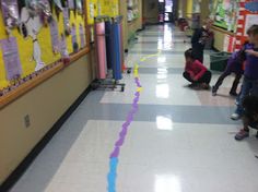 children are playing with colored tape on the floor in a school hallway while adults watch