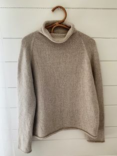 a sweater hanging on a white wall with a wooden hanger in front of it