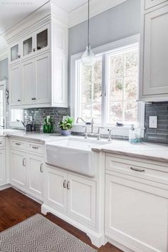 a kitchen with white cabinets and gray tile backsplash, wood flooring and an area rug