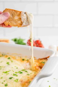 someone is dipping cheese into a casserole in a white dish with parsley on top