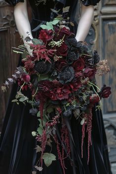 a woman in a black dress holding a large bouquet of red and purple flowers with greenery