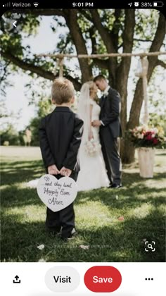 a little boy standing in front of a tree holding a sign