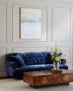 a living room with a blue velvet couch and coffee table in front of white paneled walls