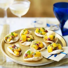 small appetizers with fruit and cheese are on a plate next to wine glasses