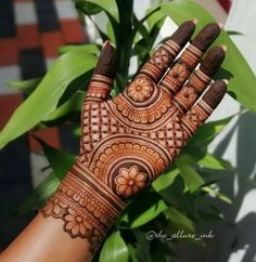 a woman's hand with henna on it and green plants in the background