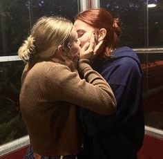 two women standing next to each other in front of a window with the lights on