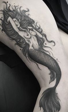 a woman's thigh with a mermaid tattoo on her leg and long hair in the shape of a tail