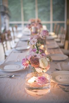 a long table with flowers in vases and plates on the tables are lit by candles