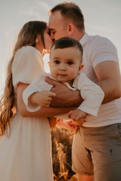 a man and woman holding a baby in their arms while standing next to each other