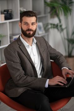 a man with a beard is sitting in a chair and using a laptop while looking at the camera