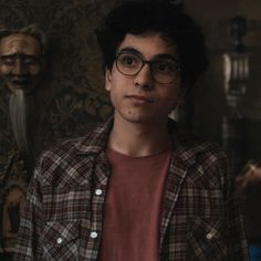 a young man wearing glasses standing in front of a wall with carved heads on it