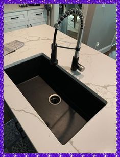 a kitchen sink with a black faucet and marble counter top in the middle