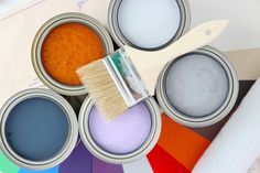 four paint cans with different colors of paint and a brush on the top of them