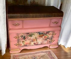 a pink dresser sitting on top of a hard wood floor next to a white curtain