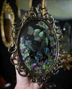 a person holding up a small mirror with butterflies on it and purple flowers in the background