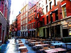 an empty street with tables and benches in front of buildings on both sides, surrounded by tall red brick buildings