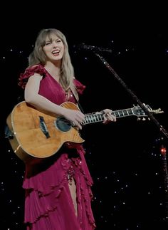 a woman in a pink dress holding a guitar and singing into a microphone on stage