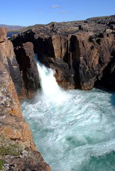 a large body of water surrounded by rocky cliff sides and green grass on the side