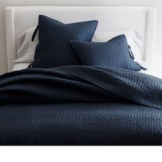 a bed with blue sheets and pillows on it's headboard in a bedroom