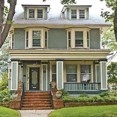 a blue house with white trim and green shutters on the front porch, surrounded by trees