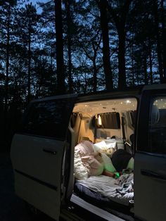 the back end of a white van with its doors open and people sleeping in it