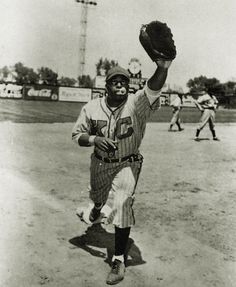 an old black and white photo of a baseball player holding a glove in the air