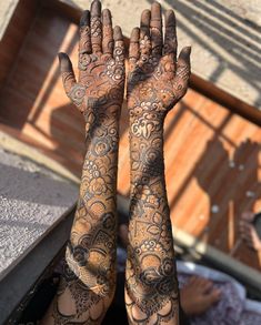 two hands covered in hendi with intricate designs on their palms and arms, both holding something up to the sky