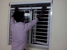 a man is looking out the window with his hands on the bars and holding onto the blinds