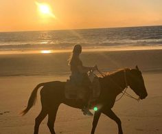 a woman riding a horse on the beach at sunset