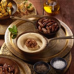 an assortment of nuts and other food items on gold plates with spoons, salt and pepper shakers