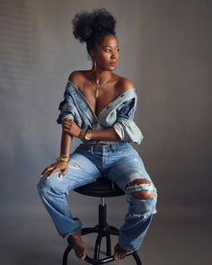 a woman sitting on top of a stool wearing ripped jeans and gold bracelets, with her arms crossed