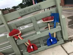 several different colored brushes are on display in front of a wooden fence that says kids at work