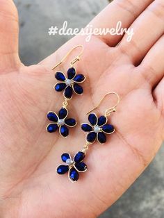 a pair of blue flower earrings sitting on top of a hand