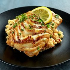 a black plate topped with chicken and rice covered in lemon wedged garnish