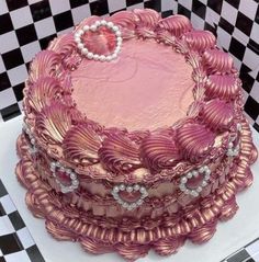 a pink cake sitting on top of a checkered tablecloth covered plate with pearls